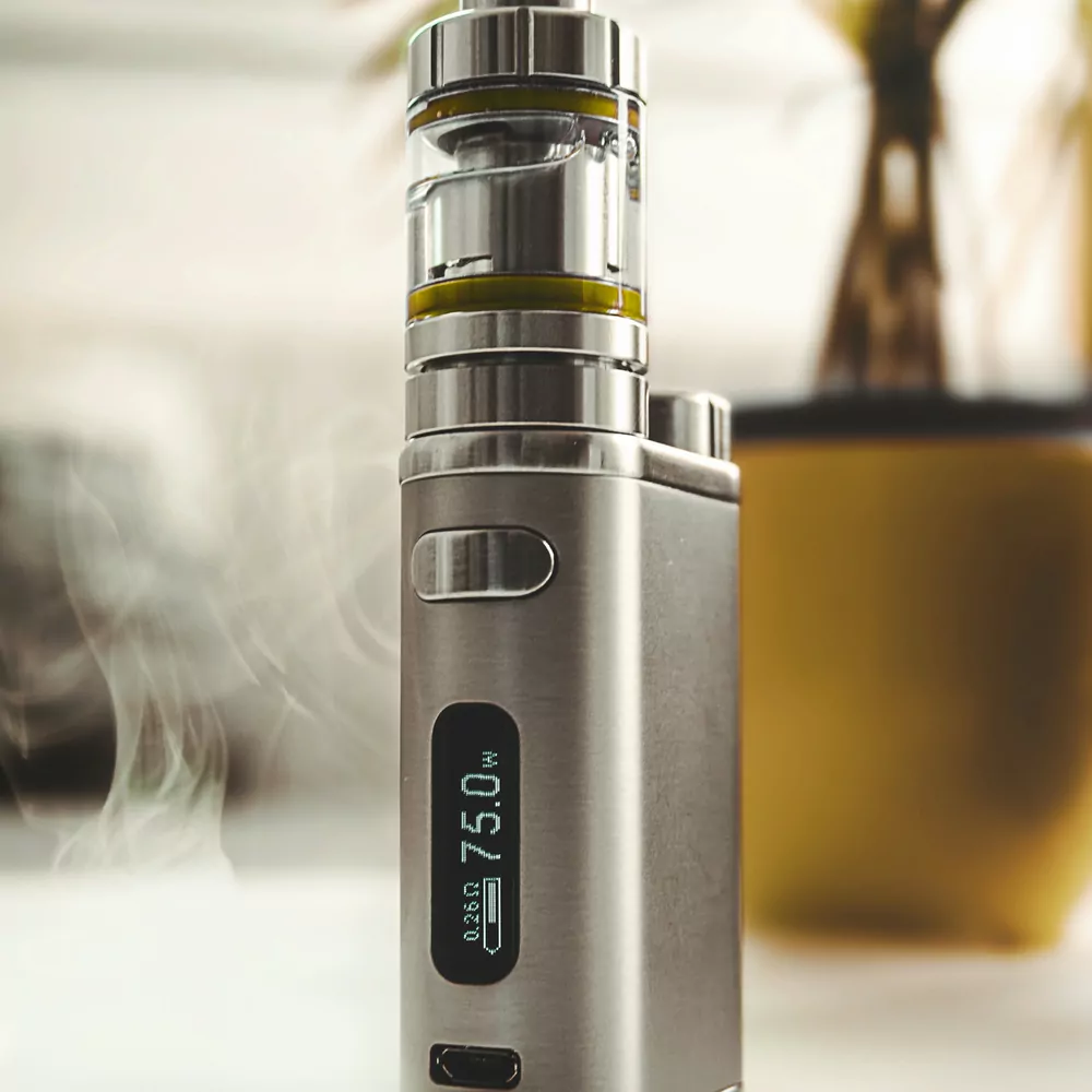 A brushed steel box mod with a tank and a small 75 watt display, standing upright