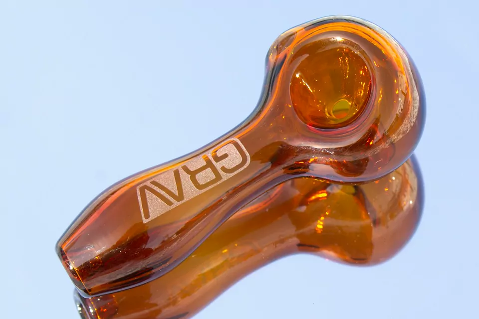 An amber glass hand pipe against a pale blue background