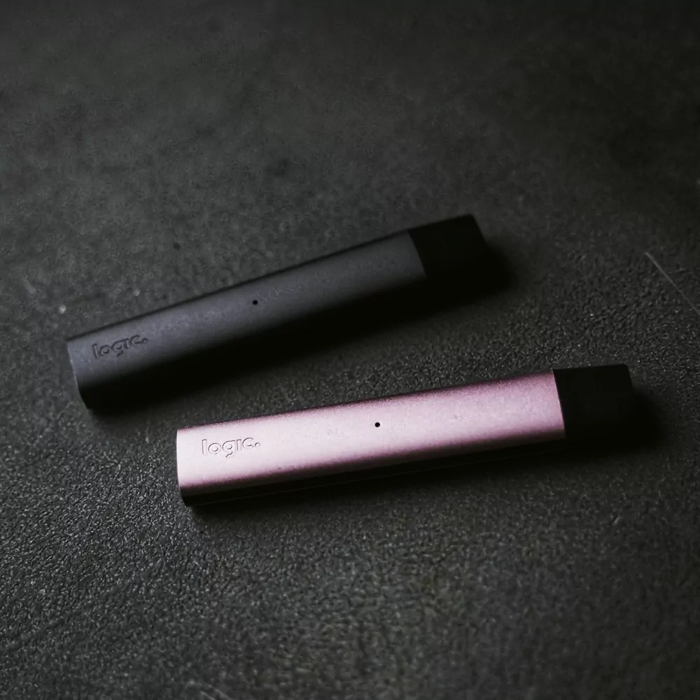 Two slim disposable vapes, one black and one pink, on a dark textured surface