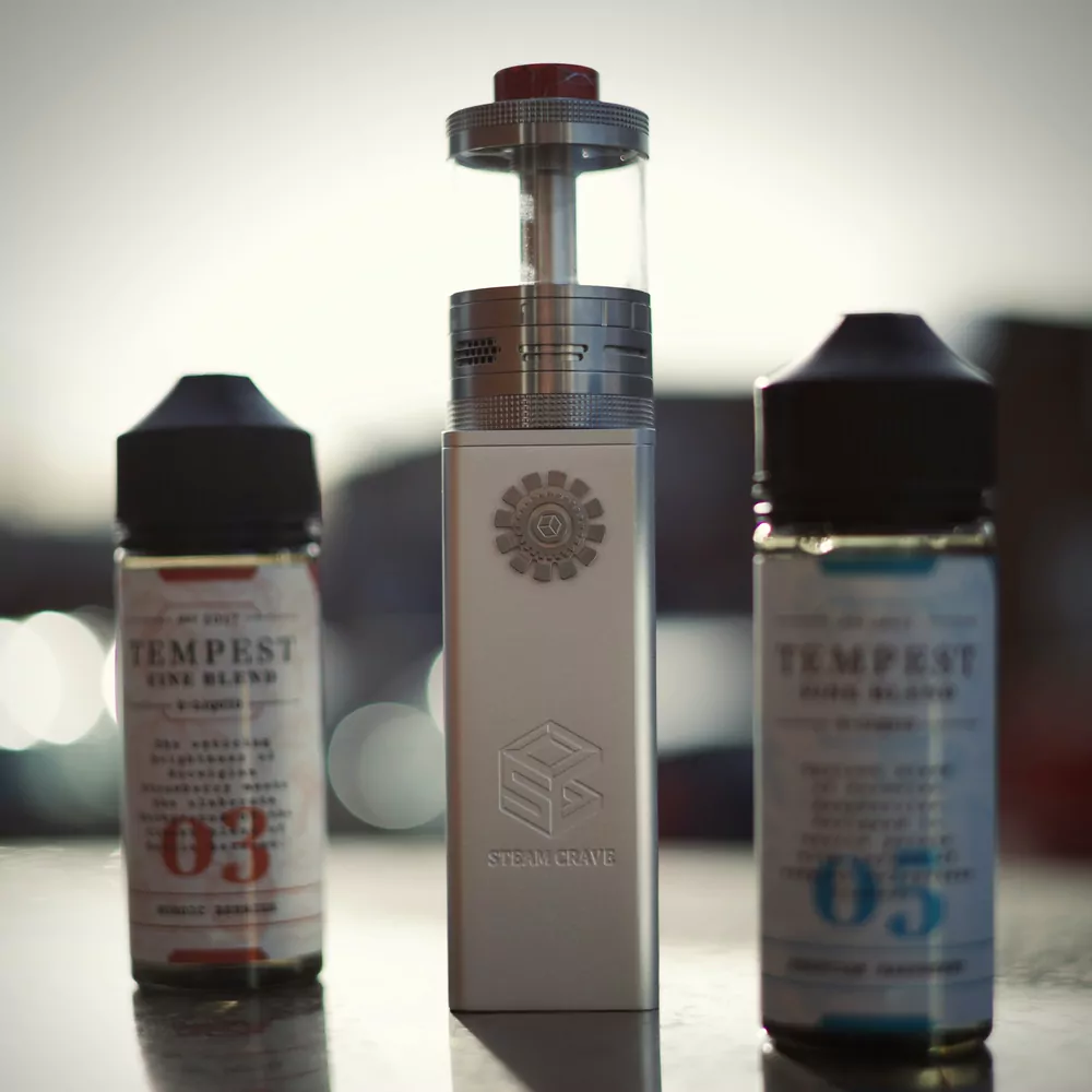 Two e-liquid bottles either side of a boxed tank, on a table