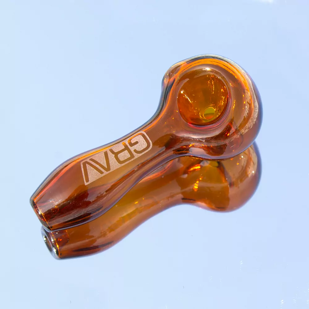 An amber glass hand pipe against a pale blue background