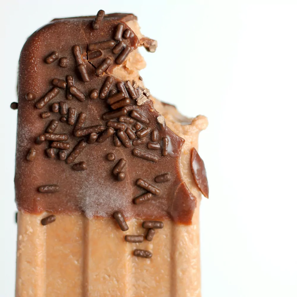 A chocolate dipped ice cream bar with chocolate sprinkles on a white background